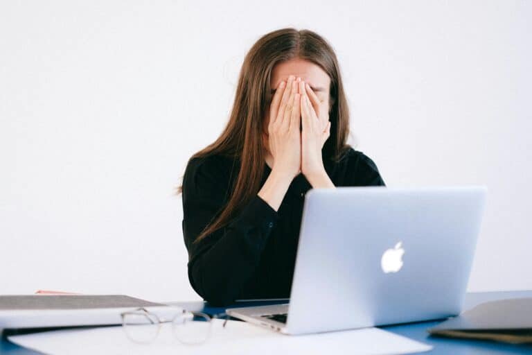Frustrated woman covering her face while sitting at a laptop – representing job loss in tech